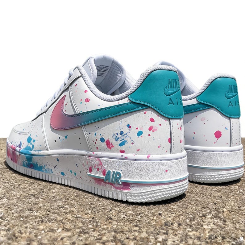 May include: White Nike Air Force 1 sneakers with teal and pink accents. The shoes feature a teal heel tab with the Nike logo, a pink and teal gradient swoosh, and colorful paint splatter details. The word "AIR" is visible on the sole.