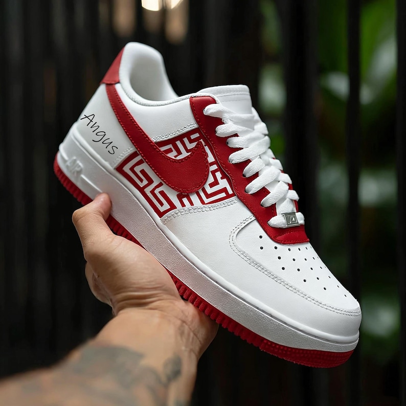 Puede incluir: Zapatilla deportiva blanca y roja con el nombre "Angus" impreso en el lateral. La zapatilla presenta un logotipo de Nike rojo y un patr&oacute;n geom&eacute;trico rojo. La suela y los detalles son rojos.