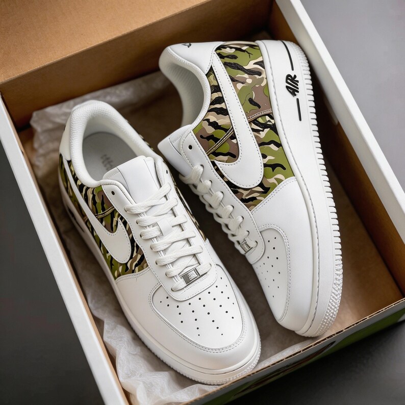 May include: White sneakers with a camouflage pattern on the side panels and heel. The shoes have a white sole, laces, and a Nike swoosh. The sneakers are in a cardboard box.