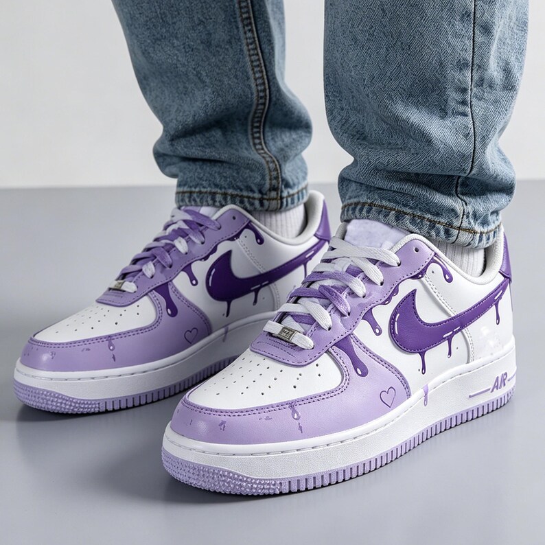 May include: White and purple sneakers with a drip design. The sneakers feature a white base with purple accents, including the Nike swoosh and a dripping paint effect. A small heart is visible on the side of the shoe.