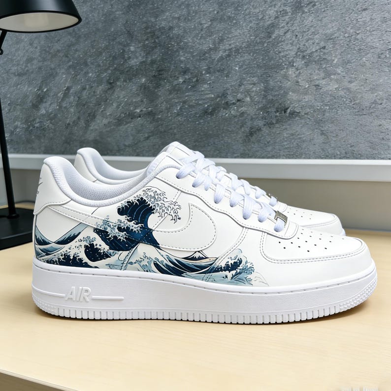 May include: White sneakers with a blue and white wave design. The shoes feature a white sole, laces, and a Nike swoosh. The wave design is inspired by Japanese art.
