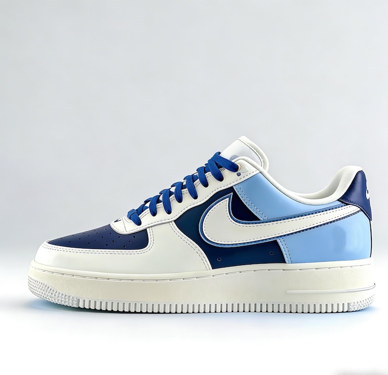 May include: A white, navy blue, and light blue Air Force 1 sneaker. The shoe features a white swoosh, blue laces, and a cream-colored sole. The heel and toe box are navy blue.