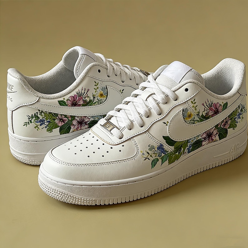 May include: White leather trainers adorned with floral patterns in pink, blue, and yellow. The trainers feature white laces, a white sole, and the Nike logo on the side.