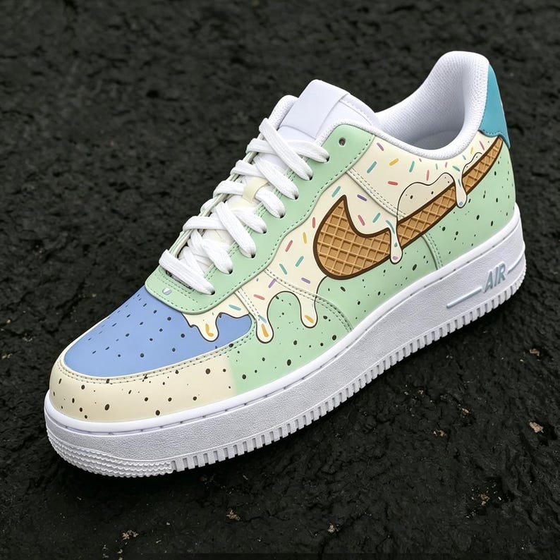 May include: Customized low-top sneaker with a unique ice cream design. The shoe features a white sole, laces, and interior. The upper is decorated with pastel colors, sprinkles, and a waffle cone swoosh. The word "AIR" is printed on the side.