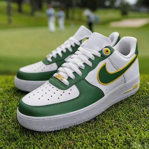 May include: White and green sneakers with a yellow swoosh logo. The shoes have white laces and a white sole. The sneakers are on a green grassy surface.