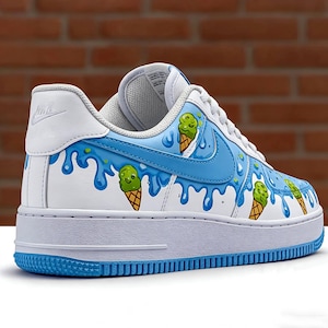 Puede incluir: Zapatillas blancas y azules con un dise&ntilde;o de cono de helado. Las zapatillas tienen una base blanca con detalles en azul, incluyendo un efecto de pintura que gotea y conos de helado de dibujos animados. El logo de Nike es visible en el lateral.