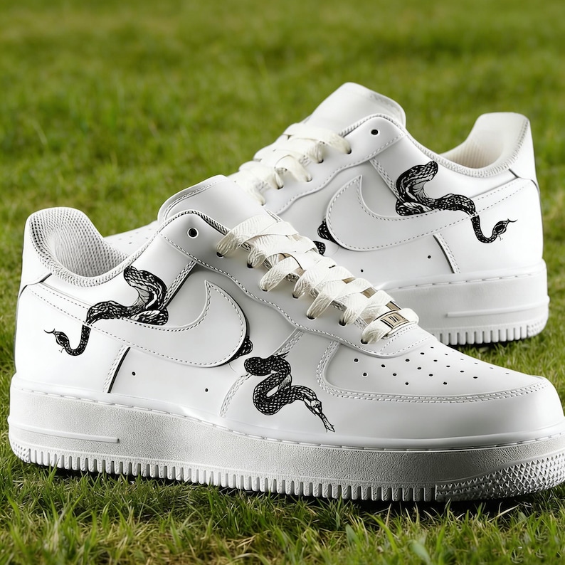 May include: White sneakers with black snake illustrations. The shoes feature a classic design with the Nike swoosh logo and a low-top silhouette. The snake graphics are detailed and add a unique touch to the footwear.