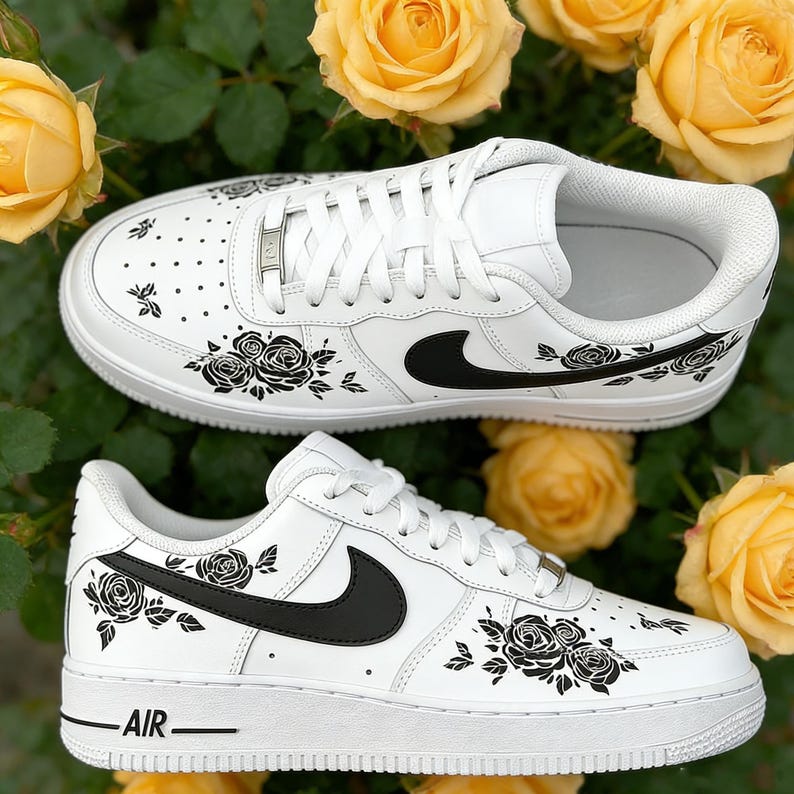 May include: White sneakers with black rose and leaf designs. The shoes feature black swoosh logos and the word "AIR" on the side. The sneakers are set against a backdrop of yellow roses.