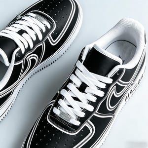 May include: Pair of black and white sneakers with white laces. The shoes have a black leather upper with white accents and a white sole. The word "AIR" is visible on the side of the shoe.