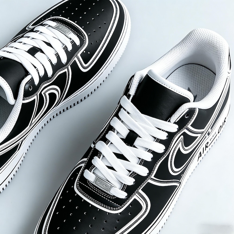 May include: Pair of black and white sneakers with white laces. The shoes have a black leather upper with white accents and a white sole. The word "AIR" is visible on the side of the shoe.