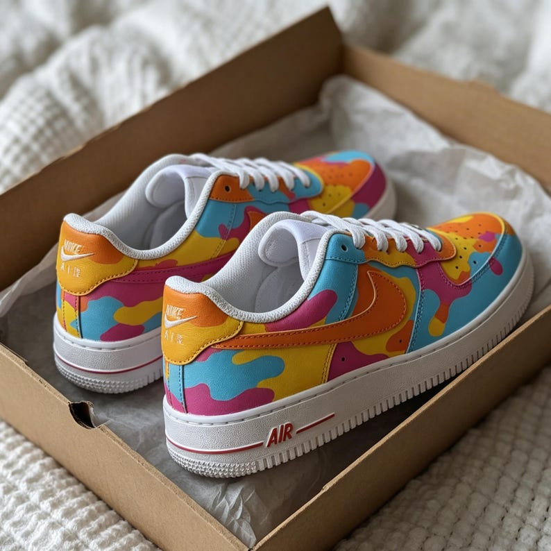 May include: A pair of colorful sneakers with a camouflage pattern in shades of orange, yellow, pink, and blue. The shoes have white laces, a white sole, and the word "AIR" in red. The Nike logo is visible on the side.