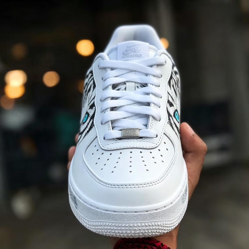 May include: White athletic shoe with black and white zebra stripe design on the sides. The shoe features a teal eye design and silver accents. The laces are white, and the sole is white.