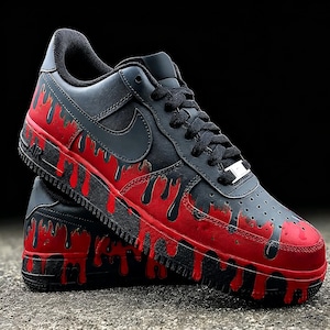 May include: Black and red Air Force 1 sneakers. The shoes feature a black base with a red dripping paint design on the midsole and toe. The Nike swoosh is black, and the laces are black.