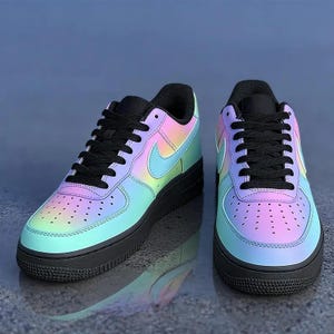May include: Pair of iridescent sneakers with a gradient of colors, including pink, blue, and yellow. The shoes have black laces, a black sole, and a Nike swoosh logo on the side. The sneakers are displayed on a reflective surface.