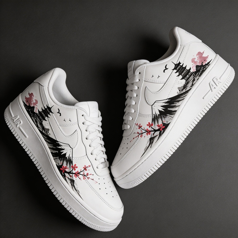 May include: White sneakers with a custom design featuring a Japanese landscape. The design includes a mountain, pagoda, and cherry blossoms in black, pink, and red. The shoes have white laces and soles, with "AR" printed on the side.