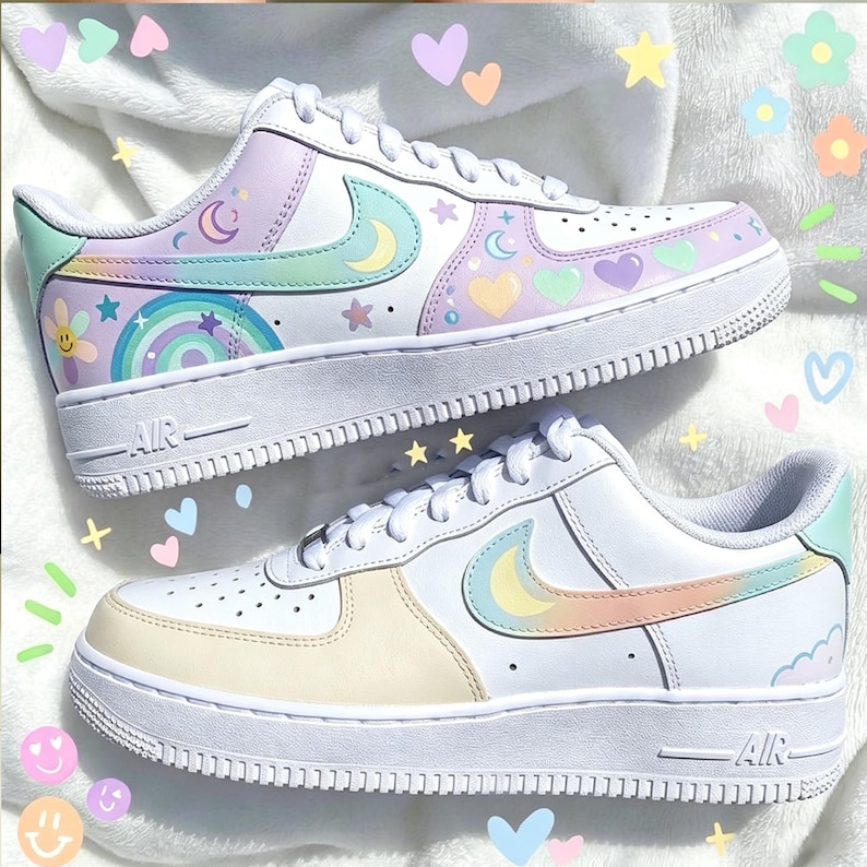 May include: A pair of white sneakers with pastel-colored accents. The shoes feature a design of moons, stars, hearts, and rainbows. The Nike swoosh is in a pastel color. The soles are white.