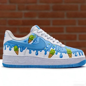 Puede incluir: Zapatillas blancas y azules con un dise&ntilde;o de helado personalizado. Las zapatillas presentan un logotipo swoosh azul claro y un efecto de pintura que gotea, con gr&aacute;ficos de conos de helado verdes. La suela es blanca con ribete azul.