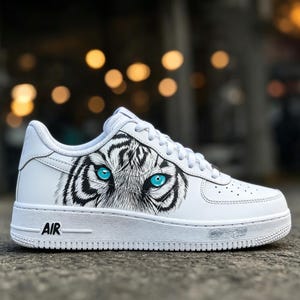 May include: White athletic shoe with a tiger eye design. The shoe features a black and white tiger eye graphic with bright blue eyes on the side. The word "AIR" is printed on the side of the sole.