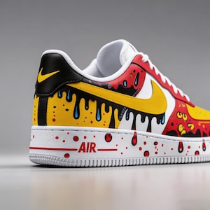 Puede incluir: Una zapatilla Air Force 1 personalizada. La zapatilla presenta una suela blanca con detalles rojos y la palabra "AIR". La parte superior es una mezcla de rojo, amarillo, negro y blanco con un dise&ntilde;o de pintura goteando. Un logo Nike amarillo es visible en el lateral.