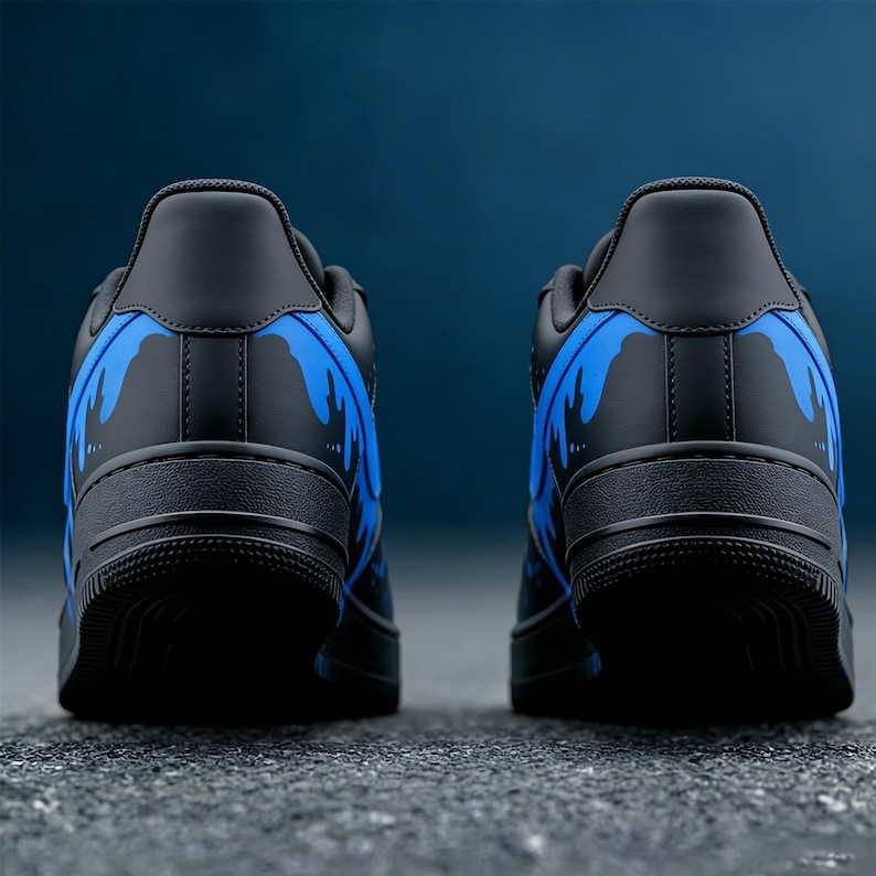 May include: Pair of black sneakers with blue flame-like designs on the back. The shoes are low-top and have a solid black sole. The background is a gradient of dark blue.