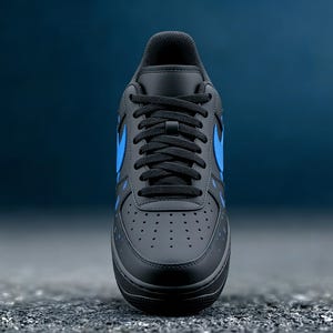 May include: Black and blue athletic shoe with a low-top design. The shoe features a black base with blue accents, including the iconic swoosh logo on the side. The laces are black, and the sole is black.