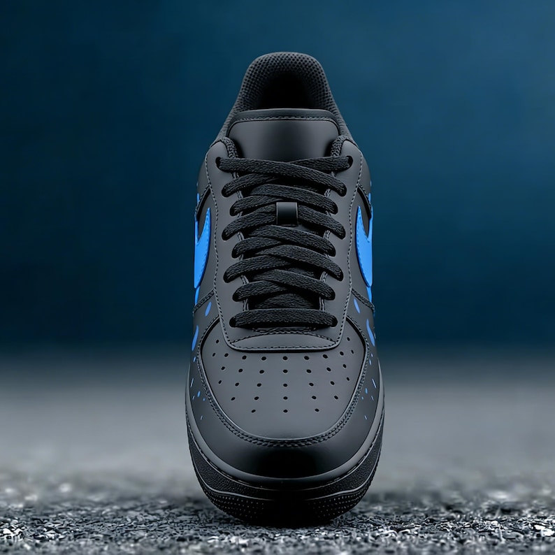 May include: Black and blue athletic shoe with a low-top design. The shoe features a black base with blue accents, including the iconic swoosh logo on the side. The laces are black, and the sole is black.