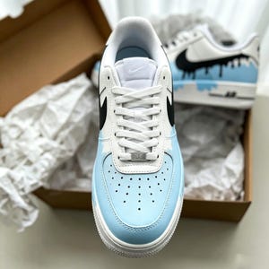 Puede incluir: Zapatillas blancas y celeste con detalles en negro. Las zapatillas tienen una puntera celeste y un dise&ntilde;o de estrella blanca en el lateral. El logo de Nike es negro. Las zapatillas est&aacute;n en una caja marr&oacute;n con papel de seda blanco.