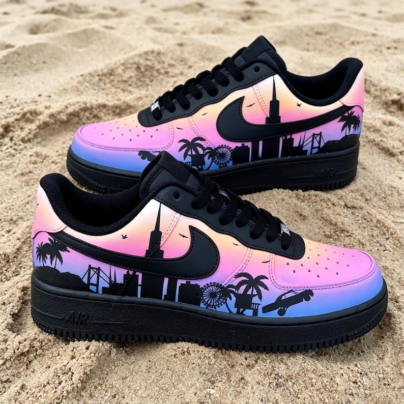 May include: Pair of black and multi-colored sneakers with a city skyline design. The sneakers feature a gradient of pink, orange, and blue hues. The black design includes palm trees, a Ferris wheel, and a car. The Nike swoosh is visible on the side.