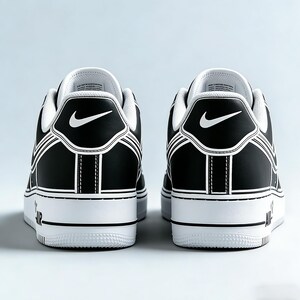 May include: Pair of black and white sneakers, viewed from the back. The shoes feature a black upper with white accents, including the Nike swoosh logo and outlining details. The white soles have "AIR" printed on the side.
