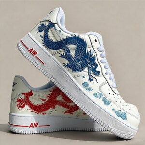 May include: White sneakers with a dragon design. One shoe features a blue dragon, the other a red dragon. The word "AIR" is printed in red on the white sole. The sneakers have white laces and a white upper.