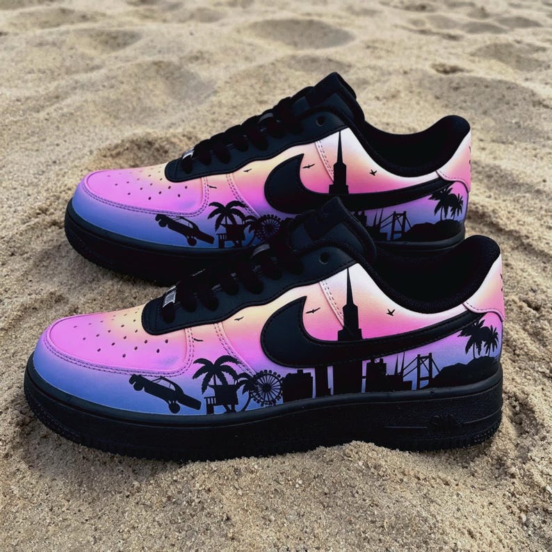May include: Pair of black and multi-colored sneakers with a city skyline design. The shoes feature a gradient of pink, purple, and blue, with black accents and a black sole. The design includes palm trees, a Ferris wheel, and a car.