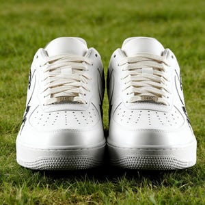 May include: Pair of white leather sneakers with cream-colored laces and a textured sole. The sneakers have a low-top design with perforations on the toe box and black accents. Each shoe features a metallic tag with the text "41K".