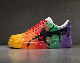 May include: A low-top sneaker featuring a vibrant rainbow gradient color scheme transitioning from yellow at the toe to purple at the heel. A black drip pattern overlays the midsection, accented by a black swoosh, red laces, and white paint splatters.