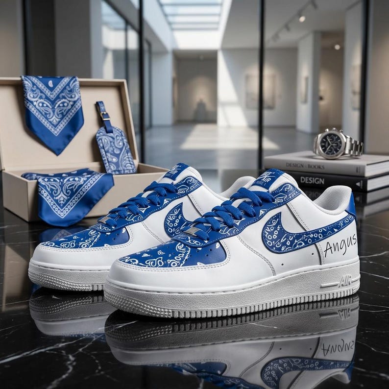 May include: White and blue sneakers with a paisley design, blue laces, and the name "Angus" on the side. A matching box set includes a bandana, tag, and necktie. A watch and books are in the background.