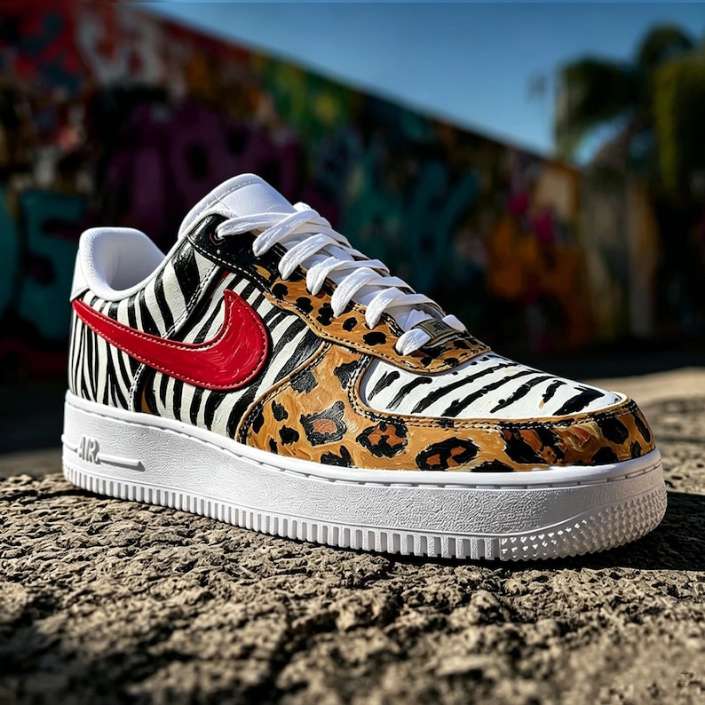 May include: A custom Air Force 1 trainer with a white sole, zebra print, leopard print, and a red swoosh. The shoe has white laces and a white tongue. The background is a colourful graffiti wall.