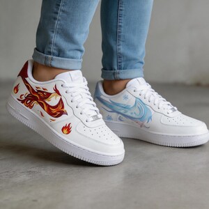 May include: White sneakers with custom artwork. One shoe features a fiery phoenix design in red, orange, and yellow. The other shoe has a blue and white winter-themed design with snowflakes. Both shoes have white laces and soles.