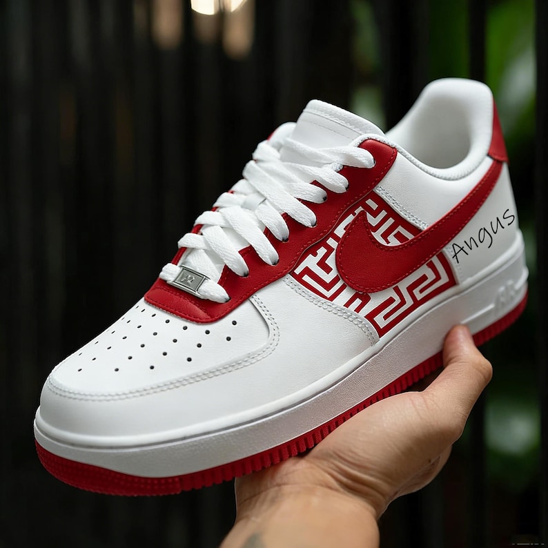 Puede incluir: Zapatillas Air Force 1 blancas y rojas con un logotipo rojo y un patr&oacute;n rojo decorativo. El zapato tiene cordones blancos y una suela roja. La palabra "Angus" est&aacute; escrita en el lateral del zapato.