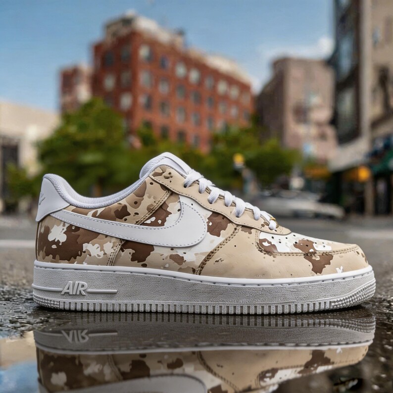 May include: A tan, brown, and white camouflage pattern Nike Air Force 1 low-top sneaker. The shoe features a white swoosh, laces, and sole. The word "AIR" is visible on the midsole.