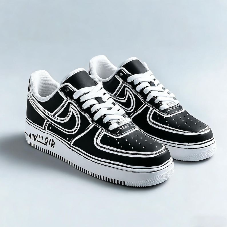 May include: Pair of black and white sneakers with white laces. The shoes have a black upper with white outlines and a white sole. The text "AIR OIR" is printed on the side of the sole. The shoes are a classic athletic style.