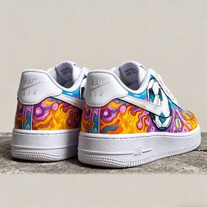May include: White Nike Air Force 1 sneakers with custom colorful artwork. The design features a soccer ball graphic and a vibrant mix of orange, purple, and blue abstract patterns. The shoes have white soles and the Nike Air logo.