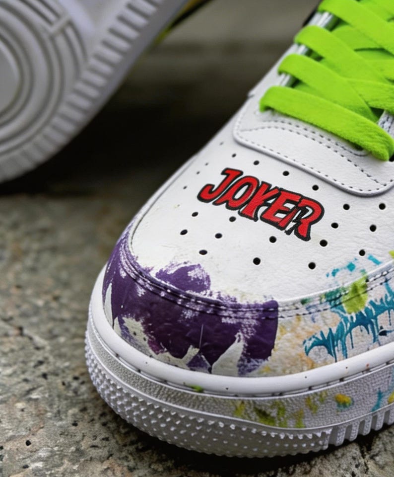 May include: White sneakers with green laces and the word "JOKER" in red lettering. The toe and sides of the shoe feature a colorful splatter paint design in purple, blue, and yellow.