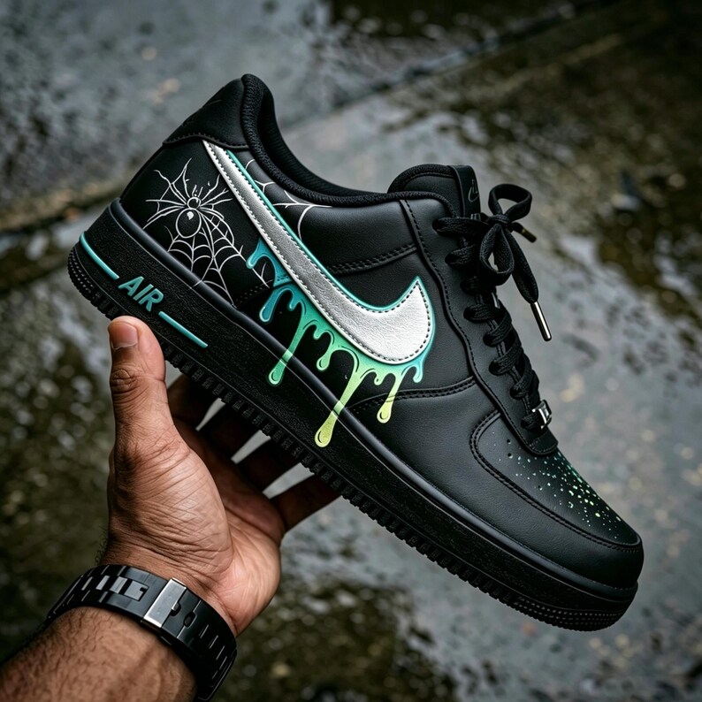 May include: Black Air Force 1 sneakers with a silver Nike swoosh and a unique design. The shoe features a spiderweb and dripping paint effect in shades of green and blue. The word "AIR" is visible on the side.