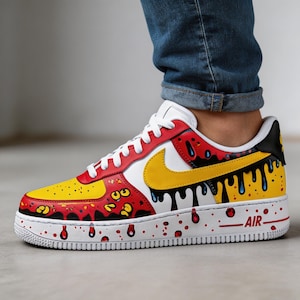 Puede incluir: Zapatillas Air Force 1 personalizadas con un dise&ntilde;o vibrante. La zapatilla presenta una combinaci&oacute;n de colores amarillo y rojo con detalles de pintura negra goteando, una suela blanca y un logotipo de Nike amarillo. La palabra "AIR" est&aacute; impresa en el lateral.