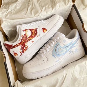 May include: Pair of white sneakers with custom artwork. One shoe features a phoenix design in red, orange, and yellow. The other shoe has a blue and white winter-themed design with snowflakes and a swoosh.