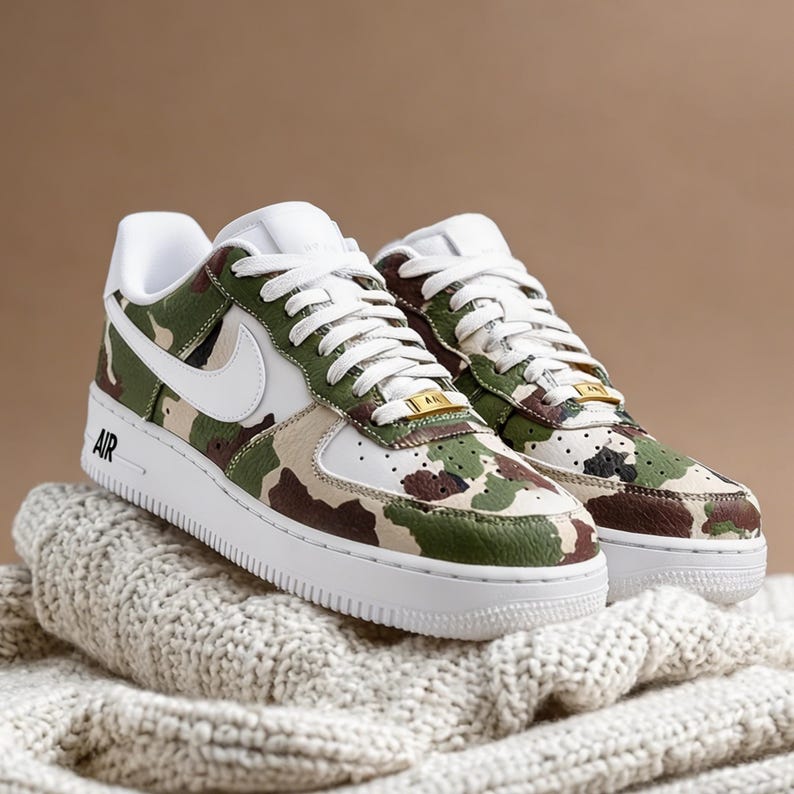 May include: A pair of camouflage-patterned sneakers with white accents, laces, and soles. The sneakers feature a green, brown, and tan camouflage design on the upper, with a white Nike swoosh and the word "AIR" on the side.