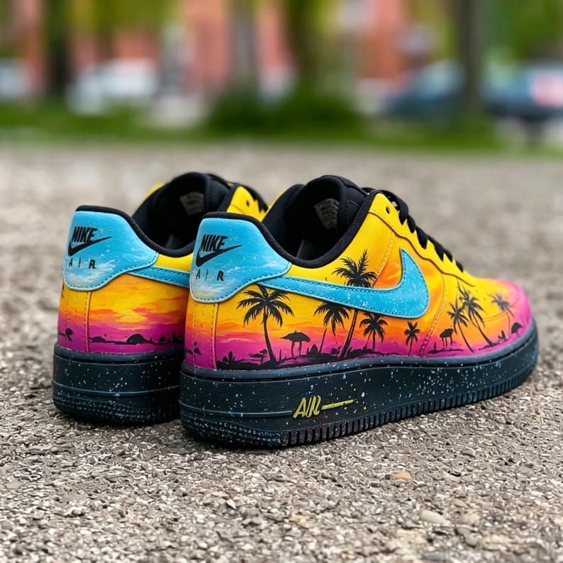 May include: Pair of Nike Air Force 1 sneakers with a vibrant sunset design. The shoes feature a yellow, orange, and pink gradient upper with black palm tree silhouettes. The Nike swoosh is blue, and the midsole is black with blue speckles.