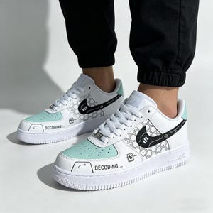 May include: White and mint green sneakers with black graphic designs and the word "DECODING..." printed on the side. The sneakers feature a white sole and a black Nike swoosh logo.