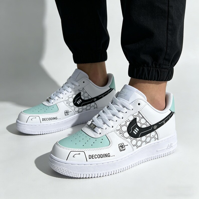 May include: White and mint green sneakers with black graphic designs and the word "DECODING..." printed on the side. The sneakers feature a white sole and a black Nike swoosh logo.