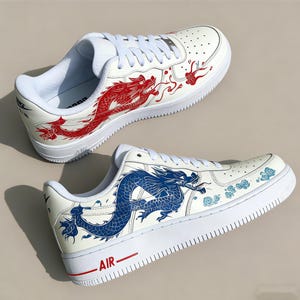 May include: White sneakers with red and blue dragon designs. The shoes feature a classic low-top design with white laces and soles. The word "AIR" is printed in red on the side of the shoe.