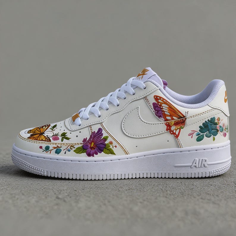 May include: White leather sneaker with floral and butterfly designs. The shoe features a white sole and laces, with colorful illustrations of butterflies and flowers on the sides. The word "AIR" is visible on the sole.